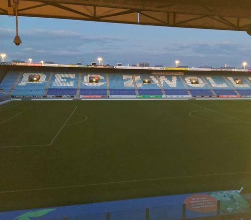 Foto van de grasmat en een deel van de tribune van het stadion van Pec Zwolle, in het avondlicht