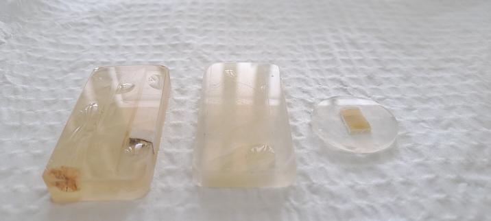 Three sets of rock samples mounted in resin. The two on the left are large (about 50 mm by 24 mm) and the rocks are pale yellow. The one on the right is small (about 24 mm in diameter). All three are reflecting light.
