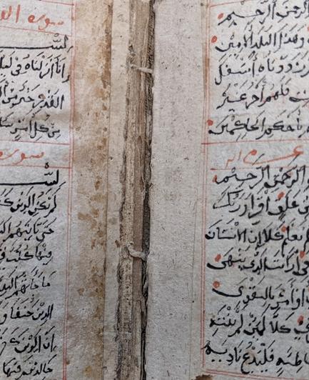 The gutter of an Islamic book showing small linen thread stitches stabbed through the section folds. Remnants of discoloured animal glue repairs on left side.