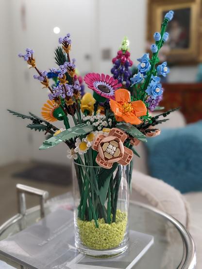 Glass vase with light green pebbles and assembled LEGO Flower Bouquet and Wildflower Bouquet sets inside.