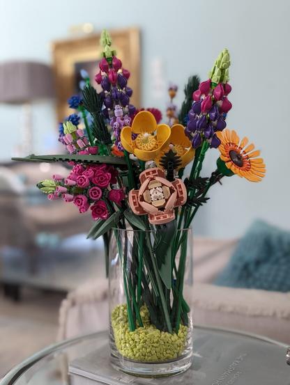 Glass vase with light green pebbles and assembled LEGO Flower Bouquet and Wildflower Bouquet sets inside.