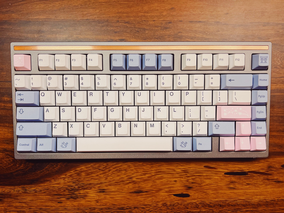Gray 75% keyboard with copper accent bar at the top, with gray, white and pink keycaps