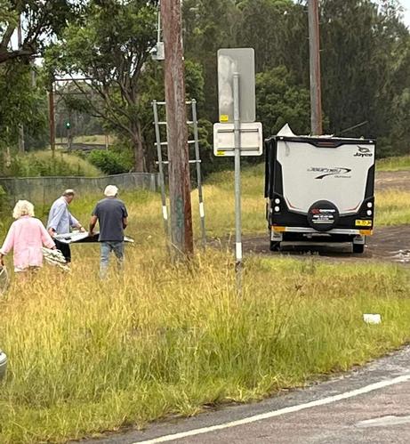 An older lady in pink and two older men enjoying team work and exercise in the fresh air as they carry part of their caravan roof back to their caravan.