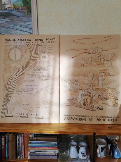 Two sandy coloured embroidered panels mounted on stretchers and propped up on top of a bookcase. You can't see them very well, because there's a slash of strong sunlight across them.