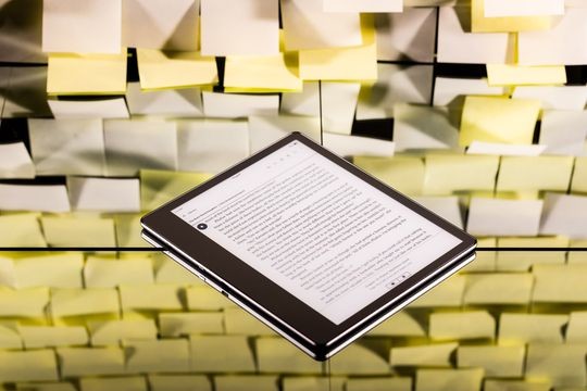 A tablet with an ebook on it's display. In the background is s wall covered with post-its