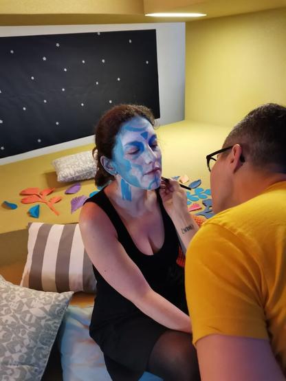 Julia Happymiaow maquillando de azul y blanco a nuestra compañera, que hoy será 99, una inteligencia artificial en prácticas