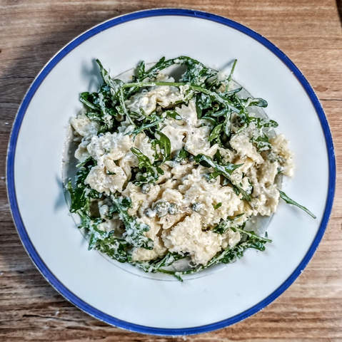 Das Gericht auf dem Teller. Man sieht Farfalle, Rukola, Erbsen und eine helle cremige Sauce.