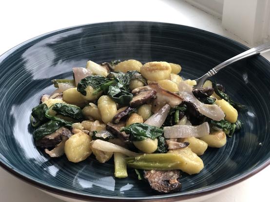 A dark blue bowl containing gnocchi, spinach and mushrooms.