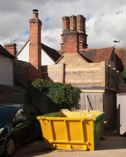 Colour vertical photograph of chimneys in striking light, with a yellow skip in the foreground. To the very right of the image is an unusual whale weather vane.