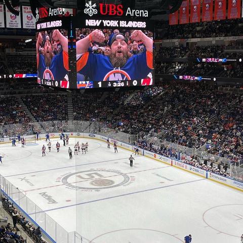 AEW pro wrestler John Silver appears on the UBS Arena Jumbotron, flexing his big, meaty, muscular arms.