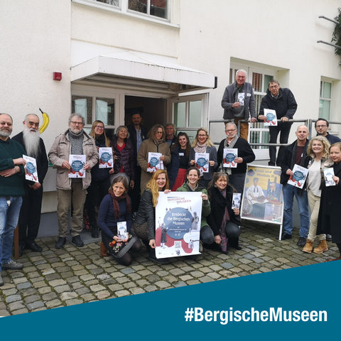 Die Mitglieder des Netzwerks Bergische Museen vor dem Eingang zum Wilhelm-Fabry-Museum mit Plakaten und Broschüren des Netzwerks.
