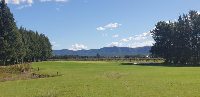 A view down the fairway of the 14th hole at Hunter Valley Golf Club with the Brokenback Range in the background. A clear blue sky with some fluffy white clouds.