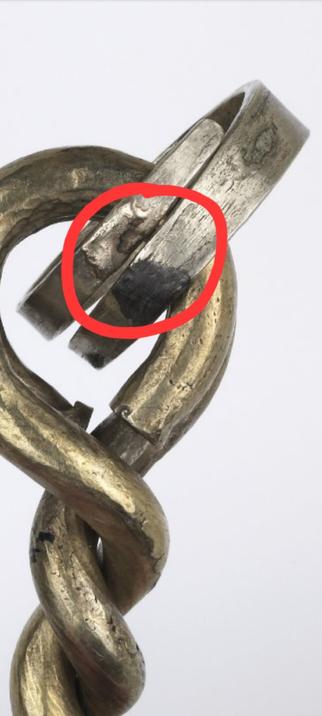 Gold 2 bar twist torc with a silvery ring attached. The ring has spashes of molten metal on.