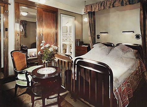 Color photo of a stateroom aboard the Kungsholm, 1926. The "double" bed is actually two single beds with separate frames pushed together. There is a small round table at the end of the beds, with a vase of fresh flowers. The room includes a mirror (to make it look larger), mahogany paneling, and a tasteful chair.