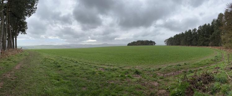 A panoramic view across a green field towards some hills covered in mist
