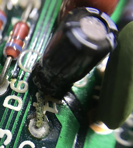 Extreme close up of the mainboard of an Olivetti M10. Image is a capacitor that is failing. Green corrosion on the legs.