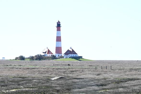 Der rotweiß gestreifte Leuchtturm von Westerhever steht mit seinen beiden Leuchtturmwärterhäusern auf einer Warft im Deichvorland mitten zwischen Salzwiesen