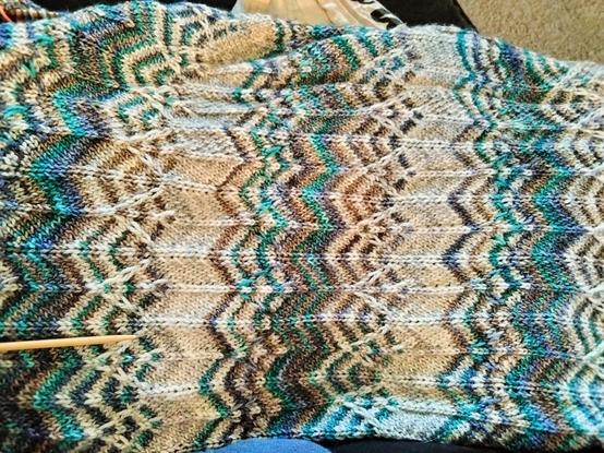 A piece of knitted material in gray, blue, green, and brown featuring a pattern of stripes and chevrons
