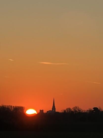 looking over a field to see the sun rise just cresting the horizon, the Cathedral is just to the right of the sun. The whole sky is orange with glow.