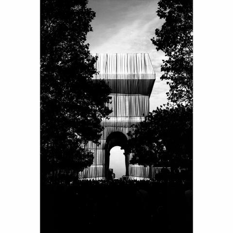 Photo en noir et blanc de l'Arc de Triomphe de la Place de l'Etoile à Paris, emballé à la Christo. Au premier plan, les arbres, qui entourent la place de l'Etoile et qui cachent une partie du monument. La photo a été prise avec un film Washi S, très contrasté.