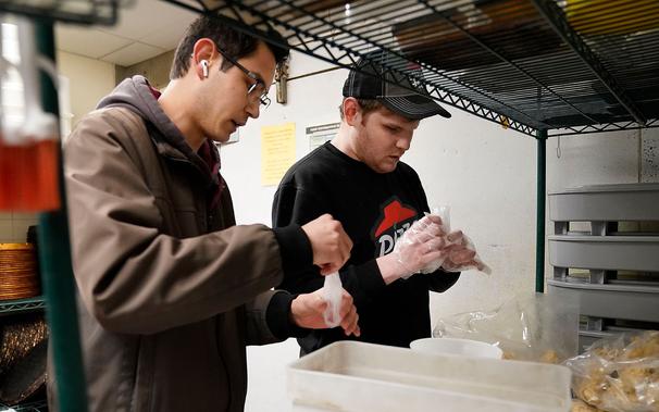 photo of two men at Pizza Hut, one sighted employee training a blind employee to bag boneless chicken wings