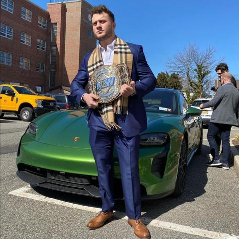 MJF poses with the AEW World Championship (a.k.a. the Triple B: Big Burberry Belt) and his own Ferrari, outside of the Oyster Bay town hall.