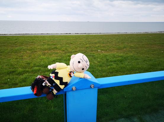 Charlie Brown und Afrolöwe auf dem Geländer der Nordsee Promenade in Norderhafen auf Nordstrand, am Horizont die Hallig Nordstrandischmoor