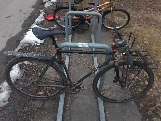 Black fixed gear bike with front rack on a bike stand with sticker.