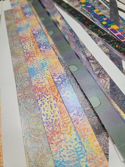 Colorful, abstract art printed on paper has been cut into long, one inch strips. The strips are piled somewhat neatly.