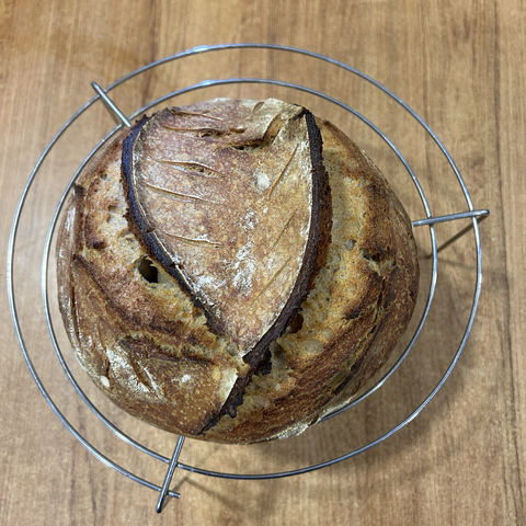 Today's sourdough loaf, still hot from the oven, on its cooling rack, seen from above. It has a gorgeous dark colour and the scoring went all right, this time.