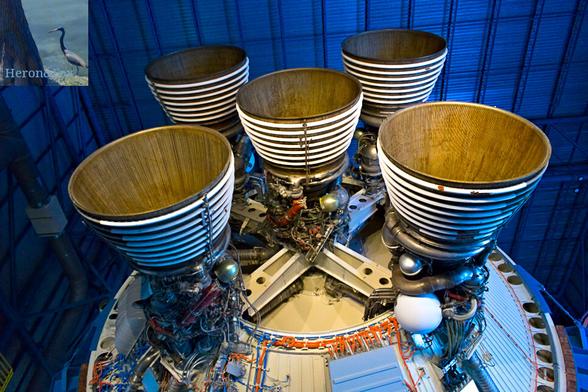 photograph of the 5 engines on the second stage of the Saturn 5 rocket. They are arranged in an X shape with one in the center. Many wires and pipes connect to the engines.