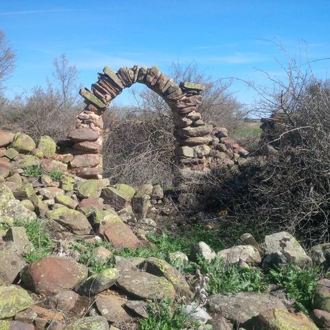 Arco de medio punto, de piedra, de aspecto rústico (no señorial) que es lo único que se mantiene en pie en una zona en ruinas. Podría ser parte de un corral. Al frente se ven unas piedras grandes hundidas, de aspecto redondeado, como si fueran cantos del río, pero en gigante.