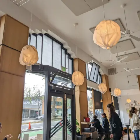 The interior of Kantine in San Francisco. Organic looking fabric ball lights hang down from a beige ceiling, big windows to the outside, and brown supports.
