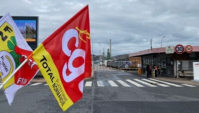 Devant l'entrée, déserte, de la raffinerie, les drapeaux des syndicats 
Au centre de l'image le drapeau CGT Total plateforme Normandie
