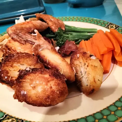 Roast dinner of roast potatoes, carrot batons, broccoli and roast chicken on a cream porcelain plate with a green tile brim