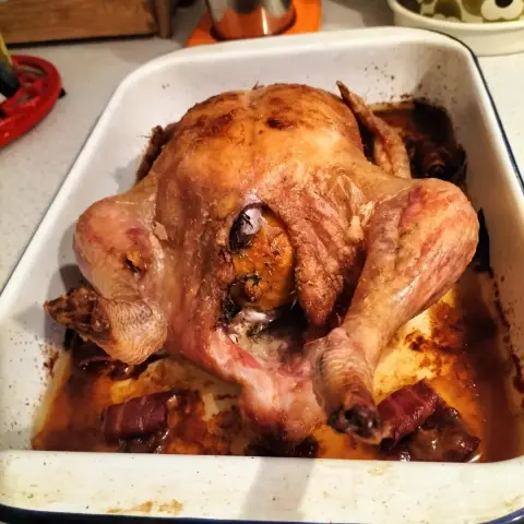 Whole roast chicken stuffed with lemon and cooked with bacon in a white enamel roasting tin