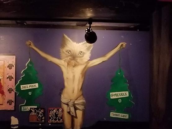 Mural of cat head on human body in crucifixion pose, holding tree automobile air fresheners