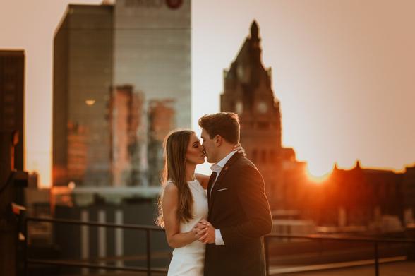 Couples embraces at sunset with the milwaukee skyline behind them.
