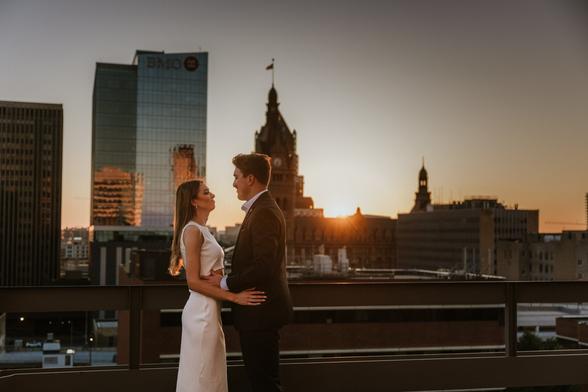 Couples embraces at sunset with the milwaukee skyline behind them.