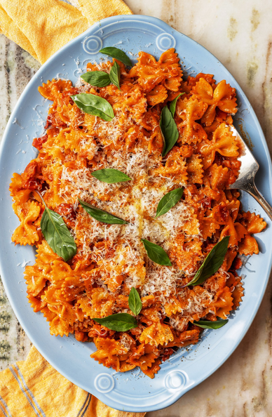 Overhead shot of a platter of farfalle pasta in a creamy tomato sauce with chickpeas in the sauce. It’s garnished with Thai basil and Parmesan cheese.