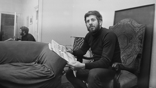 Black and white photo of actor Chaim Topol holding a newspaper.