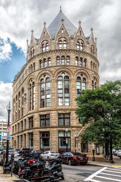 The Flour and Grain Building in  Boston, MA is now Christopher Kimball's Milk Street. It is a corner building with a rounded front and a turret that resembles a crown. The building is all stone with large, arched windows all the way around.
