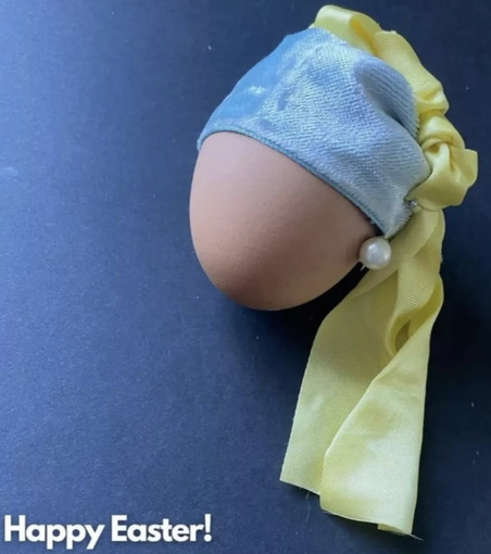 Een ei met een blauw hoofdbandje, gele sjaal eraan en een pareltje op de plek van het oor.  Is Het meisje met de parel (beroemd schilderij).