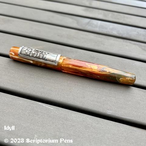 Idyll pen, capped, on picnic table. Shows full profile with custom Silver Panel Rollstop engraved with the image of a maple tree.