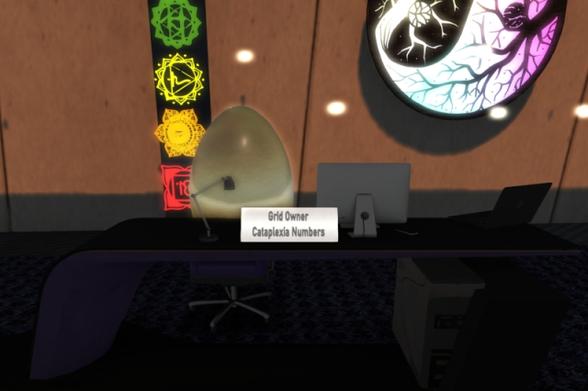Cataplexia's office desk at AMV Town Hall with a desk lamp, a computer screen and a laptop computer on it as well as a sign which reads, &quot;Grid owner&quot; and &quot;Cataplexia Numbers&quot;. A big golden egg is standing upright on the office chair.