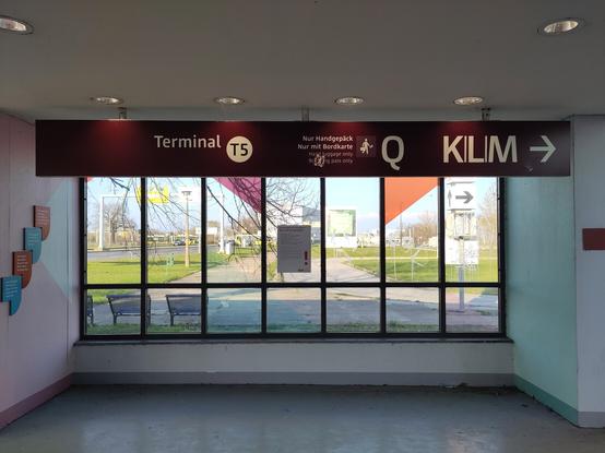 View outside through a front window at the exit of BER rail terminal 5. Hanging from the ceiling there is a a sign giving the direction to Q and KLM pointing to the right.