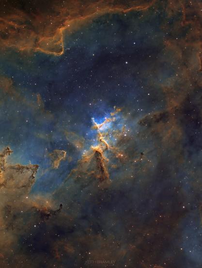 A bright Nebula embedded with stars, showing red, brown, green and orange hues