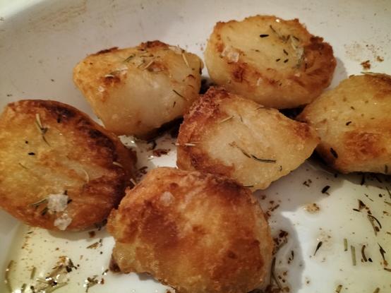 Six golden and crispy roast potatoes with garlic, rosemary and thyme in a white enamel roasting tin
