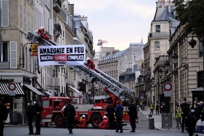 un camion de pompiers -rouge- en travers d'une rue de paris, la grue porte l'inscription : "Amazonie en feu, Macron complice"