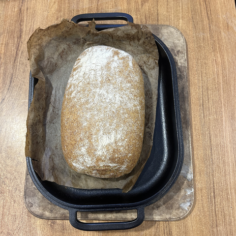 Close up from above of the bread, fresh out of the oven and still in the cast-iron bottom of mybread pan. There's baking paper between pan and bread.